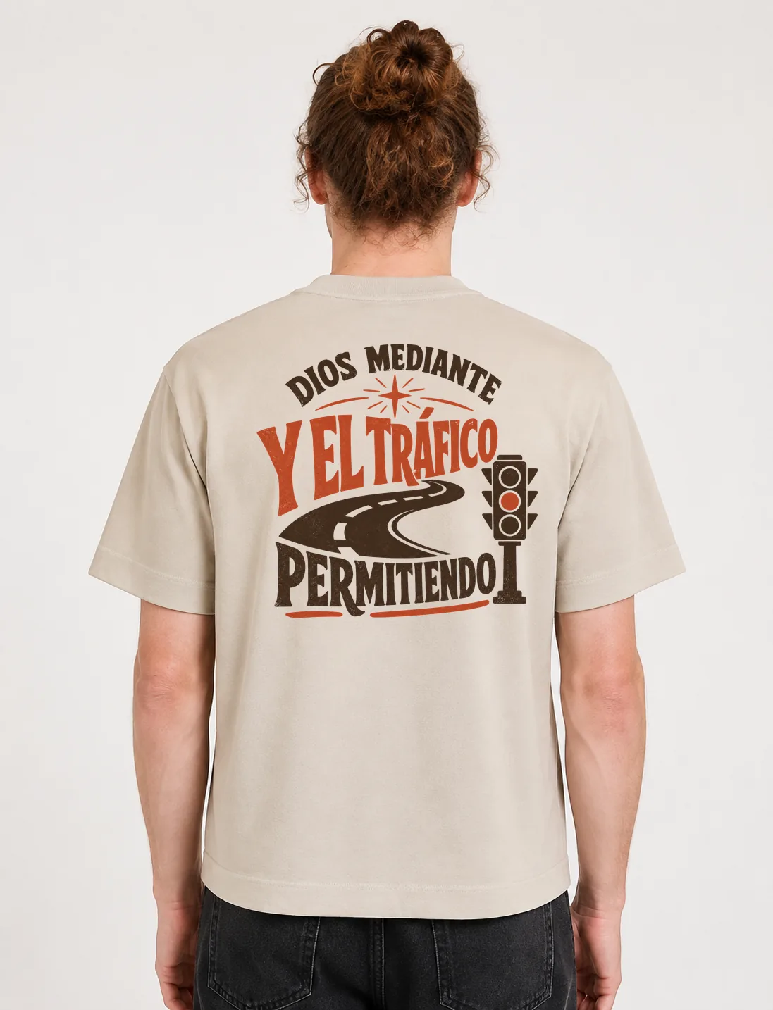 Espalda de una camiseta Cream oversized con el diseño «Dios Mediante y el Tráfico Permitiendo»: una carretera serpenteante y un semáforo junto a la frase