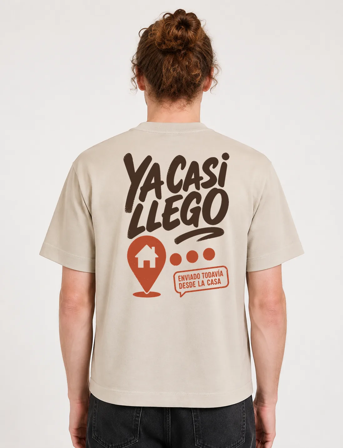 Espalda de una camiseta Cream oversized con el diseño «Ya Casi Llego»: pin de ubicación con una casa adentro y un globo que aclara que sigue en casa